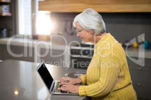 Senior woman using laptop in the kitchen