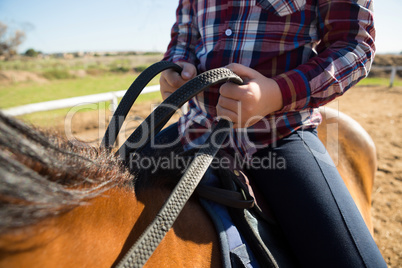 Mid section of girl riding a horse in the ranch