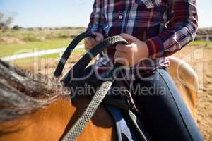 Mid section of girl riding a horse in the ranch