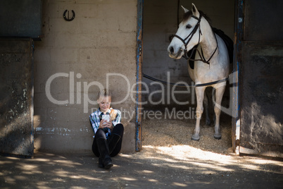 Teenage girl using mobile phone in the stable