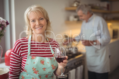 Smiling senior woman holding glass of wine in kitchen