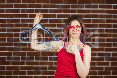 Confused woman holding hanger against brick wall