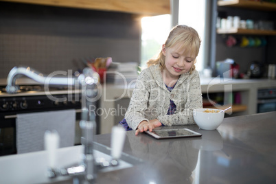 Little girl using tablet while eating cereals from a bowl