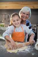 Grandmother and granddaughter posing while flattening dough