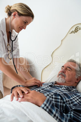 Female doctor listening to heartbeats of senior man sleeping on bed