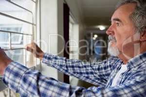 Thoughtful senior man looking through window at retirement home