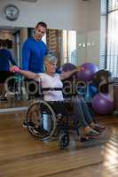 Physiotherapist assisting senior woman on wheelchair with dumbbells