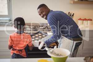 Father taking tray of fresh cookies out of oven with son in kitchen