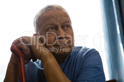 Thoughtful senior man holding walking cane while sitting at nursing home