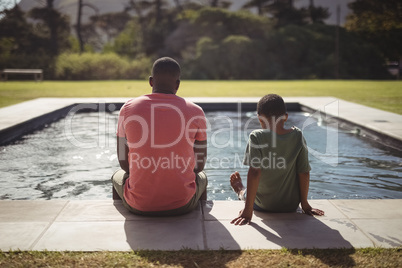 Father and son sitting on edge of swimming pool