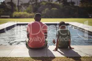 Father and son sitting on edge of swimming pool