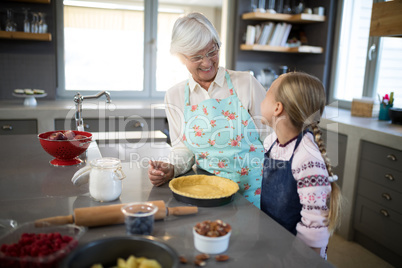 Smiling grandmother and granddaughter looking at each other while making pie