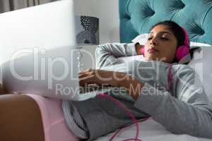 Woman using laptop while listening to music on bed