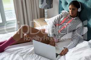Young woman using laptop while listening to music on bed