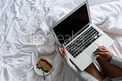 Cropped image of woman using laptop on bed