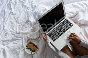 Cropped image of woman using laptop on bed