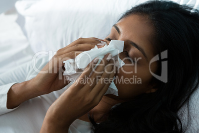 Woman blowing nose on bed