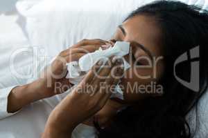 Woman blowing nose on bed