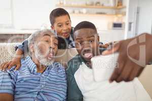 Smiling multi-generation family taking selfie from mobile phone in living room