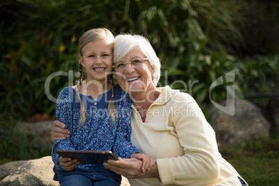 Smiling granddaughter and grandmother using digital tablet in garden