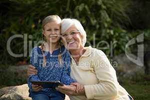 Smiling granddaughter and grandmother using digital tablet in garden