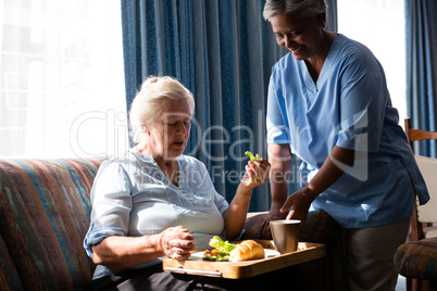 Doctor standing by senior woman eating food at table