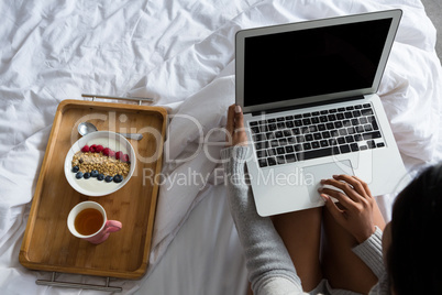 Woman with laptop by breakfast on bed