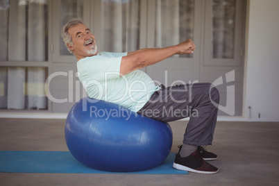 Smiling senior man doing stretching exercise on exercise ball