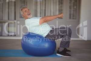 Smiling senior man doing stretching exercise on exercise ball