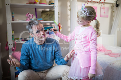 Cute daughter in fairy costume putting makeup on her fathers face