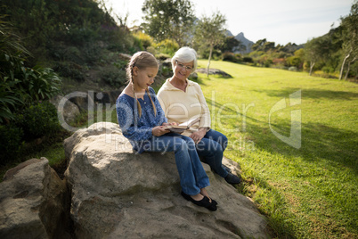 Smiling granddaughter and grandmother reading book in garden