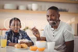 Smiling father and son having breakfast in kitchen