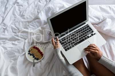 Cropped image of woman using laptop while resting on bed