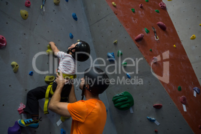 Trainer assisting boy in rock climbing