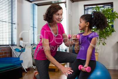 Female physiotherapist helping girl patient in performing exercise with dumbbell