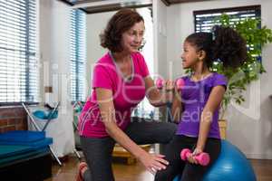 Female physiotherapist helping girl patient in performing exercise with dumbbell