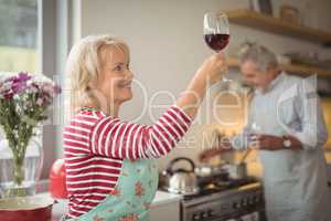 Smiling senior woman holding glass of wine in kitchen