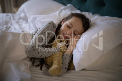 Girl sleeping on bed with teddy bear in bedroom
