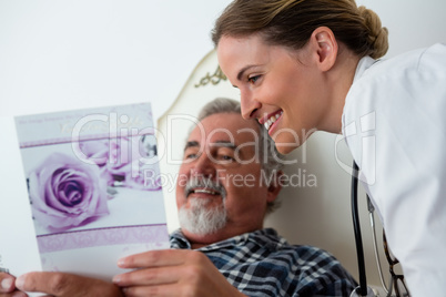 Doctor showing get well card to patient relaxing on bed