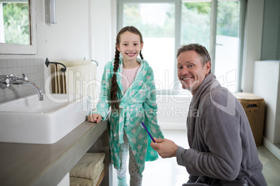 Smiling father and daughter holding toothbrush in bathroom