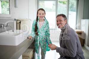 Smiling father and daughter holding toothbrush in bathroom