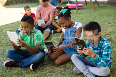 Children using tablet computer with man at park