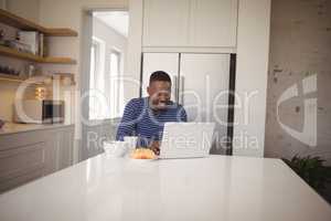 Smiling man using laptop while having breakfast in kitchen