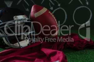 American football jersey, head gear and football lying on artificial turf against strategy board