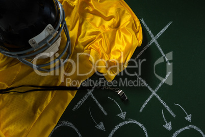 American football jersey, referee whistle and head gear lying on green board with strategy drawn on