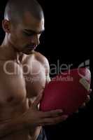 Muscular American football player looking at football in both his hands