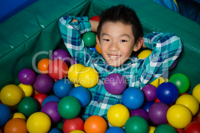 Happy boy lying in colorful balls during birthday party