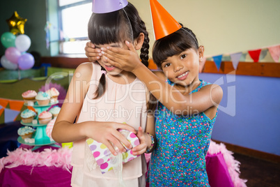 Girl covering birthday girls eyes and offering a gift