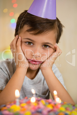 Upset boy sitting with birthday cake at home