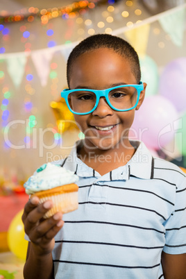 Portrait of cute boy holding cupcake during birthday party